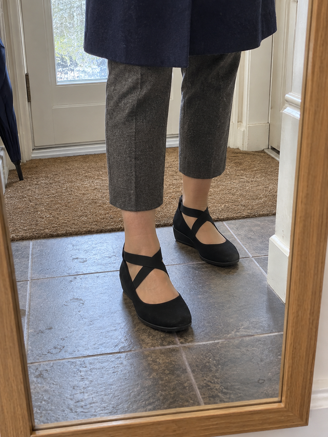 Black strapped slip-on flats with cropped grey trousers, hallway mirror photo